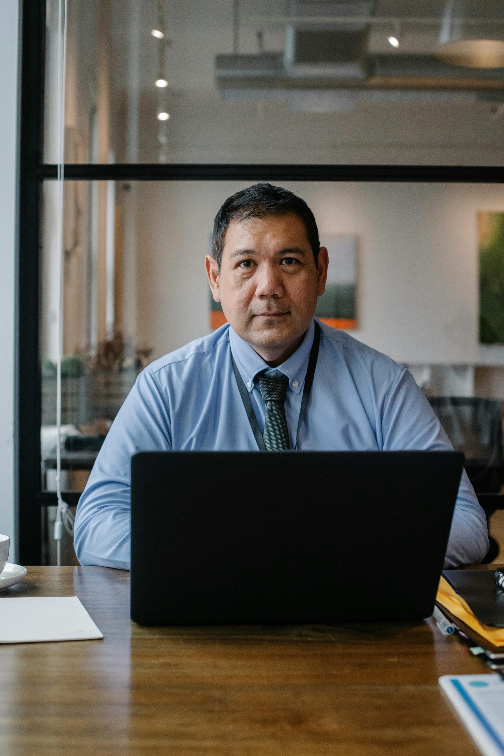 Confident ethnic man wearing formal clothes and tie working at netbook while sitting at table in workspace